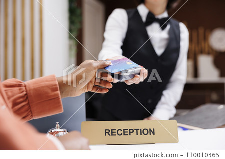 Female tourist paying at pos terminal in hotel lobby, using electronic payment at check in registration. Young resort guest using credit card at reception counter front desk. Close up. 110010365