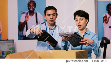 Diverse store managers preparing packages for shipping, putting stylish clothes in carton boxes in modern boutique. Employees working at clients orders, discussing delivery details in shopping mall 110010380