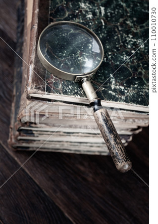 Vintage magnifying glass with books on table Vintage magnifying glass with books on table 110010730