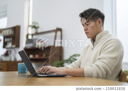 Image of a man in his 30s working from home working on a laptop 110011838