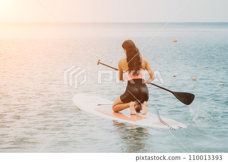 Sea woman sup. Silhouette of happy young woman in pink bikini, surfing on SUP board, confident paddling through water surface. Idyllic sunset. Active lifestyle at sea or river. 110013393