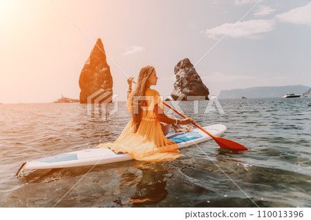 Woman sea sup. Close up portrait of happy young caucasian woman with long hair looking at camera and smiling. Cute woman portrait in bikini posing on sup board in the sea 110013396