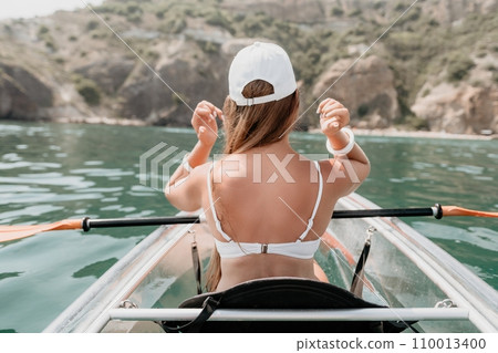 Woman in kayak back view. Happy young woman with long hair floating in transparent kayak on the crystal clear sea. Summer holiday vacation and cheerful female people relaxing having fun on the boat 110013400