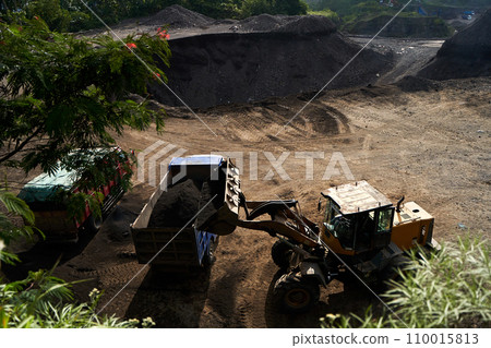 A tractor in a quarry loads minerals into a truck. 110015813