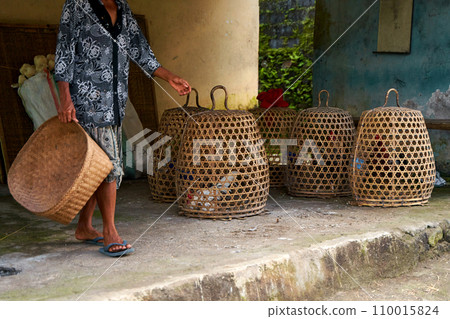 A row of straw cages for fighting roosters stands along a road in an Asian village. 110015824