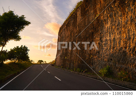 The cliff overhangs along the road to the ocean at sunset. 110015860