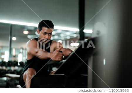 Motivated young asian sportsman having workout on rowing machine 110015923