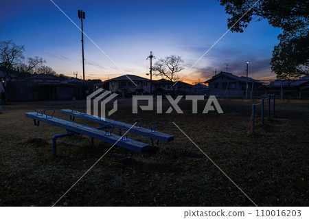 2023 A city in the dead of winter, a see-saw in a lonely park illuminated by the little remaining sunset light at dusk 2023 A city in the dead of winter, a see-saw in a lonely park illuminated by the little remaining sunset light at dusk 110016203