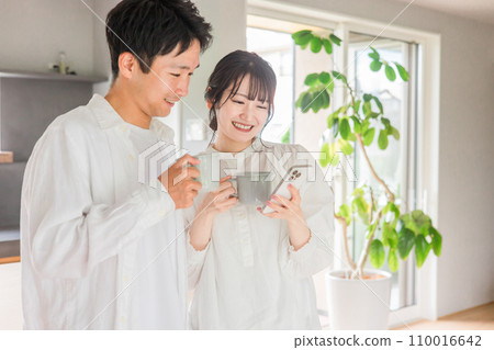 Couple looking at smartphone while drinking coffee in dining room at home Couple looking at smartphone while drinking coffee in dining room at home 110016642