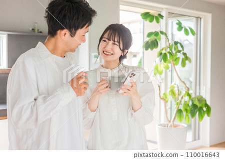 Couple looking at smartphone while drinking coffee in dining room at home 110016643