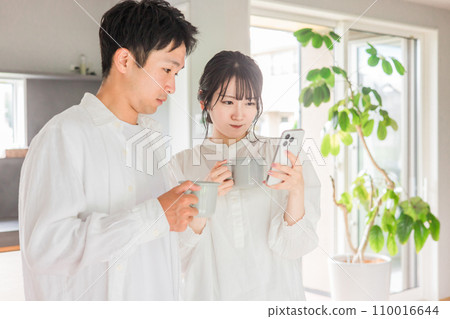 Couple looking at smartphone while drinking coffee in dining room at home Couple looking at smartphone while drinking coffee in dining room at home 110016644