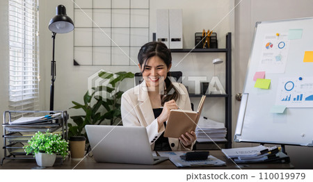 Business woman writing in a office with planning note and corporate laptop. Employee and work planner book with company paperwork Business woman writing in a office with planning note and corporate laptop. Employee and work planner book with company paperwork 110019979