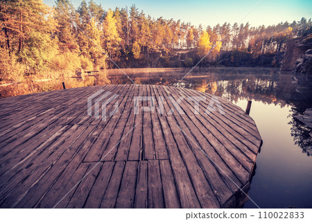 Magical sunrise over the lake. Pine trees on the lakeshore. Serene lake in the early morning. Wooden round pier on the lake. Nature landscape. 110022833