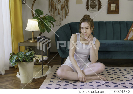 Portrait of a young brown-haired woman sitting on the living room floor 110024280