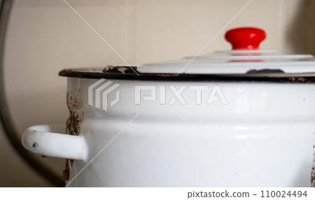 One large white pot with a lid and a red handle sits on a tile in a restaurant or home kitchen One large white pot with a lid and a red handle sits on a tile in a restaurant or home kitchen 110024494