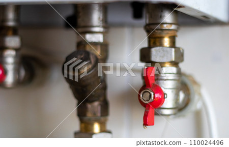 Hidden water taps for connecting a gas boiler on a tiled wall. Plumbing connections for a domestic double-circuit gas boiler. Pipes of the heating system. Installing a gas boiler with red taps Hidden water taps for connecting a gas boiler on a tiled wall. Plumbing connections for a domestic double-circuit gas boiler. Pipes of the heating system. Installing a gas boiler with red taps 110024496
