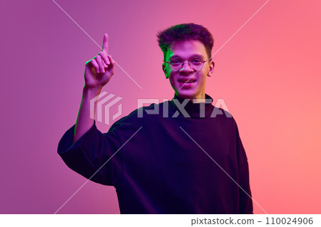 Young smiling man, student raising finger up, expressing creative ideas against gradient pink background in neon light 110024906