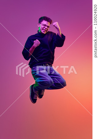 Young emotional man in casual clothes jumping and showing emotions of success, winner against gradient pink background in neon light Young emotional man in casual clothes jumping and showing emotions of success, winner against gradient pink background in neon light 110024920