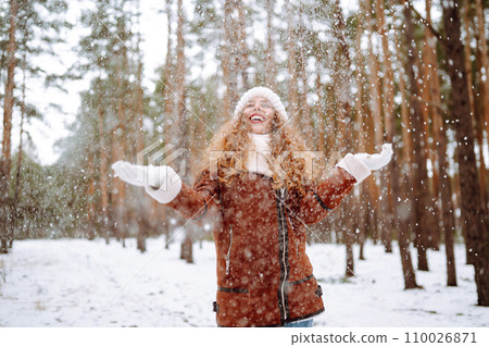 Beautiful woman standing among snowy trees and enjoying first snow. Holidays, rest, travel concept. 110026871