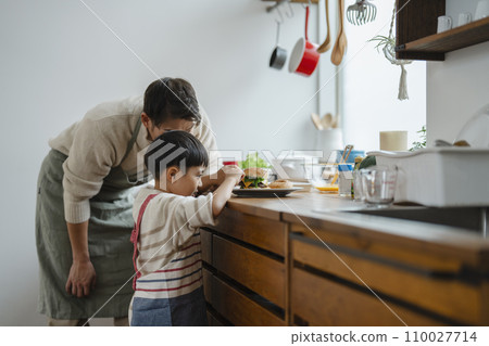 A 7-year-old boy making hamburgers in the kitchen and his father watching over him 110027714