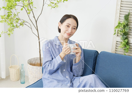 A middle-aged woman relaxing at home wearing pajamas and holding a mug A middle-aged woman relaxing at home wearing pajamas and holding a mug 110027769