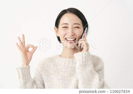 白色背景的中年婦女在用智慧型手機交談時做出「OK」手勢 110027834