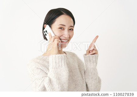 中年婦女在智慧型手機上交談時指著右側，白色背景 110027839