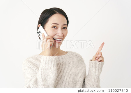 中年婦女在智慧型手機上交談時指著右側，白色背景 110027840
