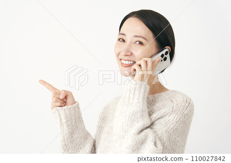 中年婦女在智慧型手機上說話時指著左邊，白色背景 110027842