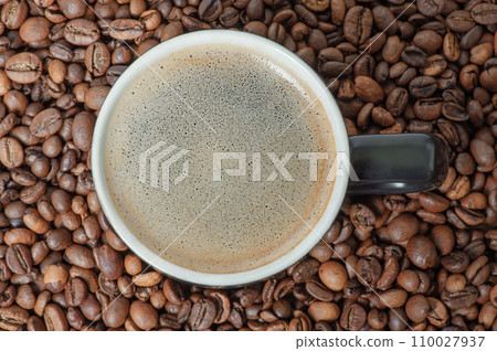 A cup of coffee on the background of roasted coffee beans. Coffee background with espresso. A cup of coffee on the background of roasted coffee beans. Coffee background with espresso. 110027937