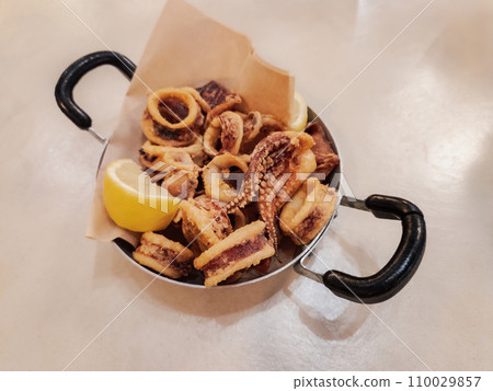 Fried squid slices served on iron cast pan with a slice of lemon. Crisply calamari tavern food concept. Fried squid slices served on iron cast pan with a slice of lemon. Crisply calamari tavern food concept. 110029857