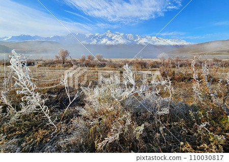 Sunny morning fog on mountain lake. Hoarfrost on grass and trees. Beautiful sunny foggy morning in the mountains. Autumn frost on dry grass. Snowy peaks in foggy clouds. Sunny morning fog on mountain lake. Hoarfrost on grass and trees. Beautiful sunny foggy morning in the mountains. Autumn frost on dry grass. Snowy peaks in foggy clouds. 110030817