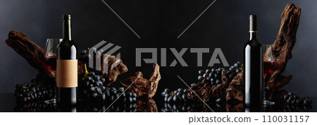 Bottles of red wine with old weathered snag and blue grapes. 110031157