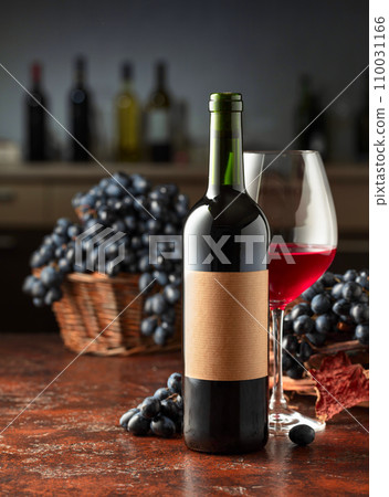 Bottle and glass of red wine with blue grapes on a vintage table. Bottle and glass of red wine with blue grapes on a vintage table. 110031166
