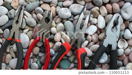 Top parts of variety types of pliers lined up in size comparison on a round smooth rocks concept photo for background or wallpapers 110031213