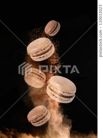 Chocolate macaroons levitate in a cloud of cocoa on a black background Chocolate macaroons levitate in a cloud of cocoa on a black background 110033023