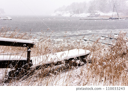 Landscape. Half frozen lake, snow coated trees. Boat pier in winter. 110033243