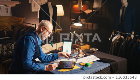 Senior craftsman shopping fabric online, using credit card at laptop in atelier. Experienced fashion designer buying material to create luxury clothing items, tailoring concept. Handheld shot. Senior craftsman shopping fabric online, using credit card at laptop in atelier. Experienced fashion designer buying material to create luxury clothing items, tailoring concept. Handheld shot. 110033548