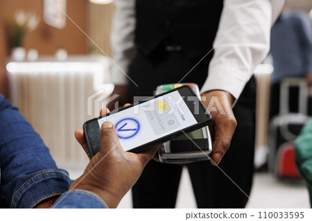 Close up of hotel guest paying with digital wallet, holding phone making mobile payment. Customer using nfc technology to pay with smartphone via pos terminal, going cashless in hospitality industry Close up of hotel guest paying with digital wallet, holding phone making mobile payment. Customer using nfc technology to pay with smartphone via pos terminal, going cashless in hospitality industry 110033595