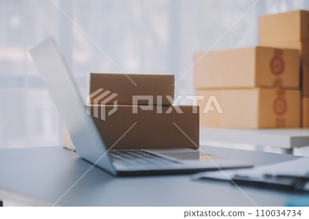 Startup small business entrepreneur or freelance Asian woman using a laptop with box, Young success Asian woman with her hand lift up, online marketing packaging box and delivery, SME concept. 110034734