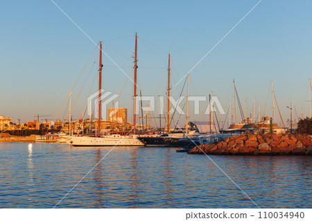 A sailing yacht with a wooden mast stands in the marina at sunset. 110034940