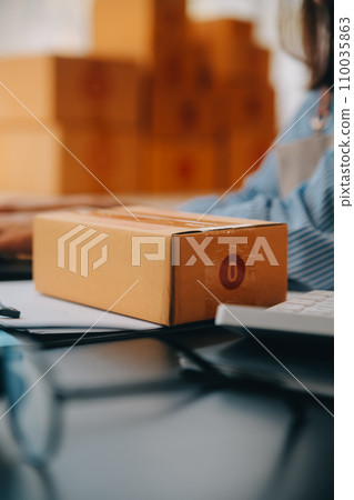 Startup small business entrepreneur or freelance Asian woman using a laptop with box, Young success Asian woman with her hand lift up, online marketing packaging box and delivery, SME concept. 110035863
