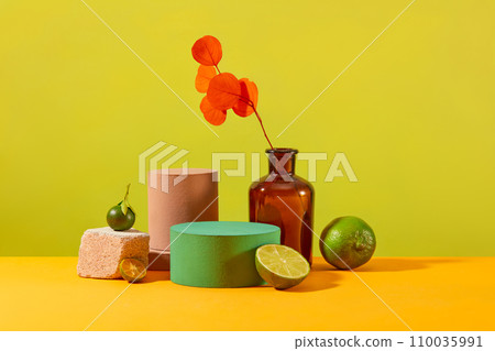 An orange leaf branch is placed in a brown vase, a round platform, fresh lemon and kumquat are placed together on a vibrant background. Empty podium for product display. Front view. An orange leaf branch is placed in a brown vase, a round platform, fresh lemon and kumquat are placed together on a vibrant background. Empty podium for product display. Front view. 110035991