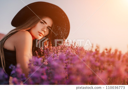 Woman lavender field. Happy carefree woman in black dress and hat with large brim smelling a blooming lavender on sunset. Perfect for inspirational and warm concepts in travel and wanderlust. Close up 110036773