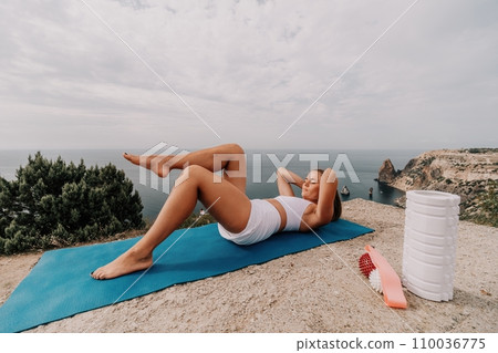 Woman sea pilates. Sporty, middle-aged woman practicing pilates in park near the sea. trains on a yoga mat and exudes a happy and active demeanor. healthy lifestyle through exercise and meditation. 110036775