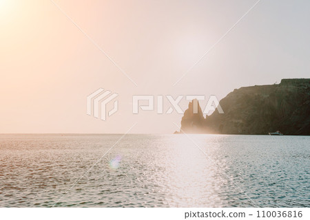 A red burning sunset over the sea with rocky volcanic cliff. Abstract nature summer ocean sea background. Small waves on golden warm water surface with bokeh lights from sun. A red burning sunset over the sea with rocky volcanic cliff. Abstract nature summer ocean sea background. Small waves on golden warm water surface with bokeh lights from sun. 110036816