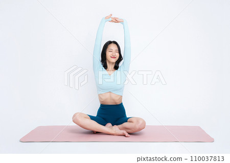 photo of a woman stretching bare body while sitting on a yoga mat 110037813