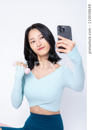 The woman sitting on the floor is taking a selfie with her phone. The woman sitting on the floor is taking a selfie with her phone. 110038649