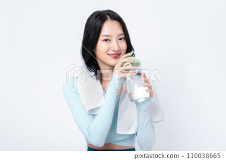 There is a woman holding a bottle of water with a towel wrapped around her neck There is a woman holding a bottle of water with a towel wrapped around her neck 110038665