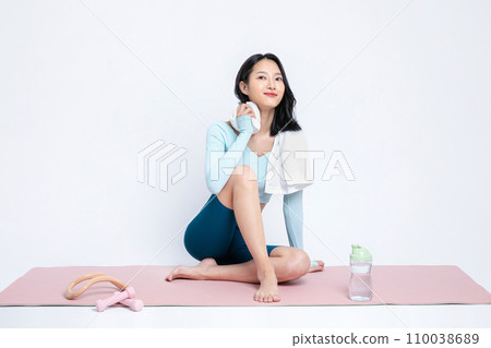 There is a woman who wipes sweat from her neck with a towel on a yoga mat There is a woman who wipes sweat from her neck with a towel on a yoga mat 110038689